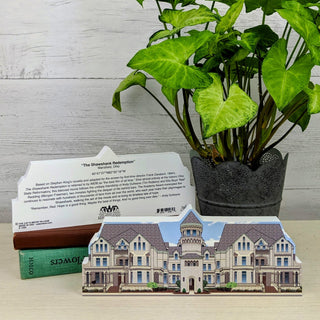 Potted plant next to a 3/4" thick wooden cutout with text and a 3D house model on a wooden surface.