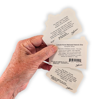 A hand holding three small paper labels or tags with printed text and barcodes, shown against a plain white background.
